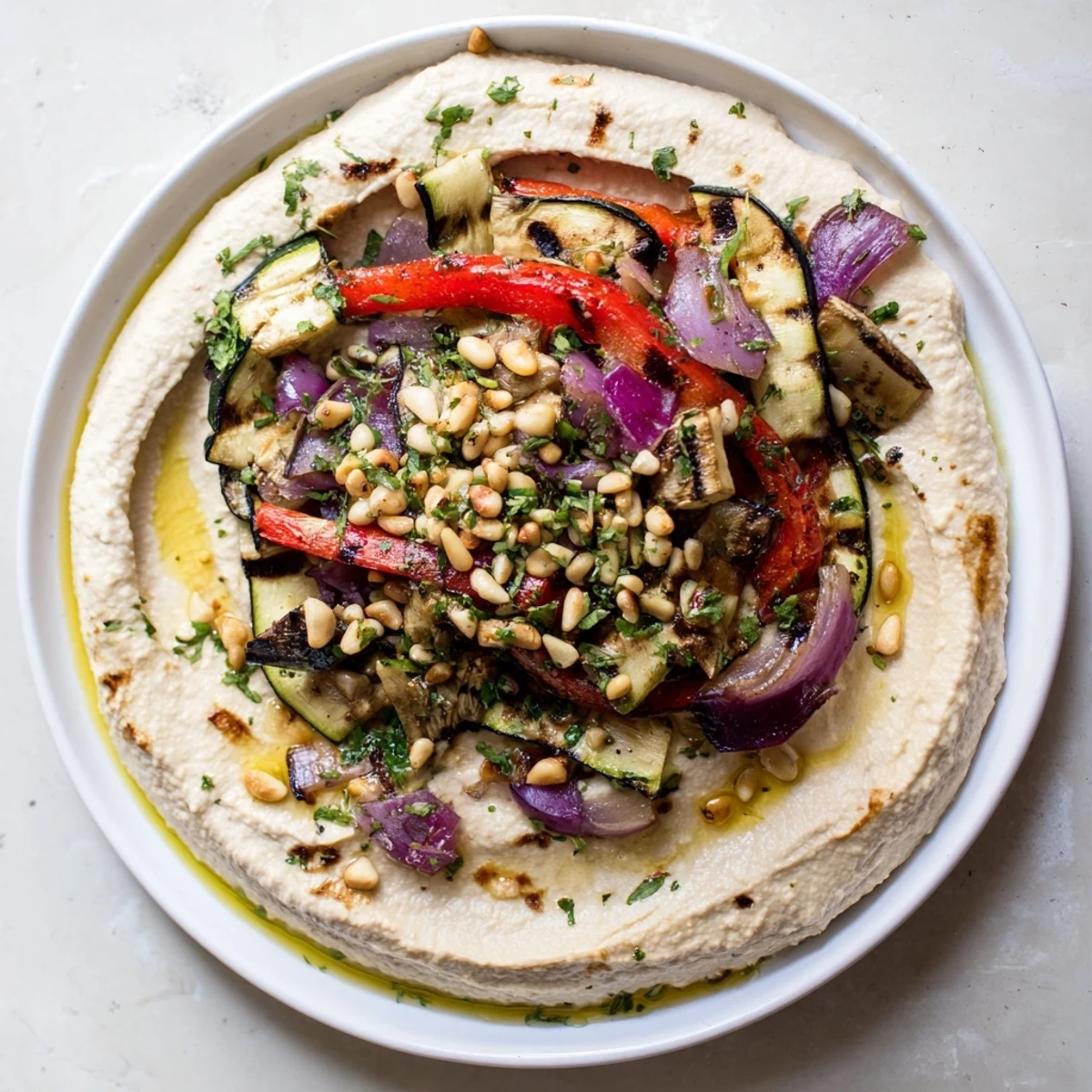 A beautiful close-up of hummus roasted veggies garnished with toasted pine nuts and fresh parsley, delicious!
