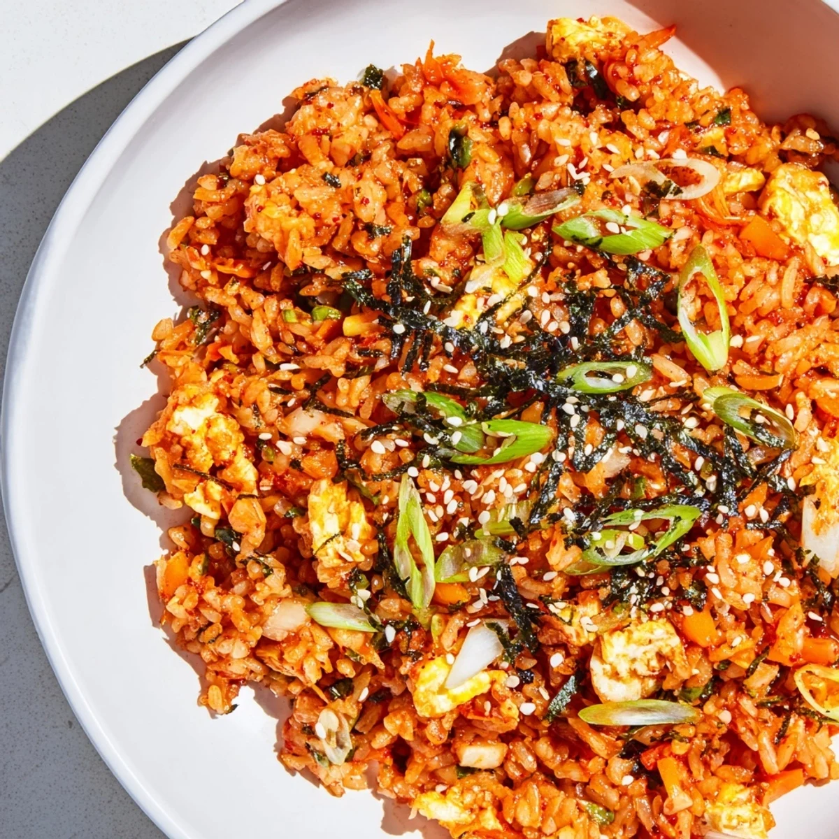 Steaming plate of Spicy Kimchi Fried Rice speckled with green onions, ready to eat with chopsticks.