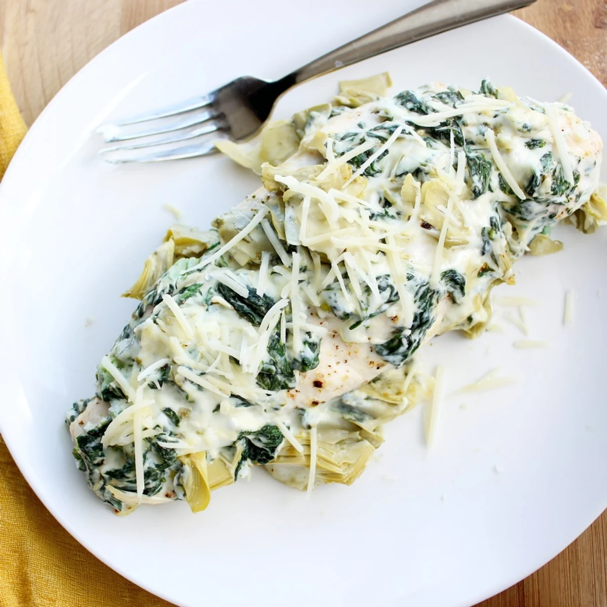 Golden-brown Spinach & Artichoke Chicken Bake served hot from the oven, with bubbly melted cheese and tender chicken breasts in a ceramic dish.