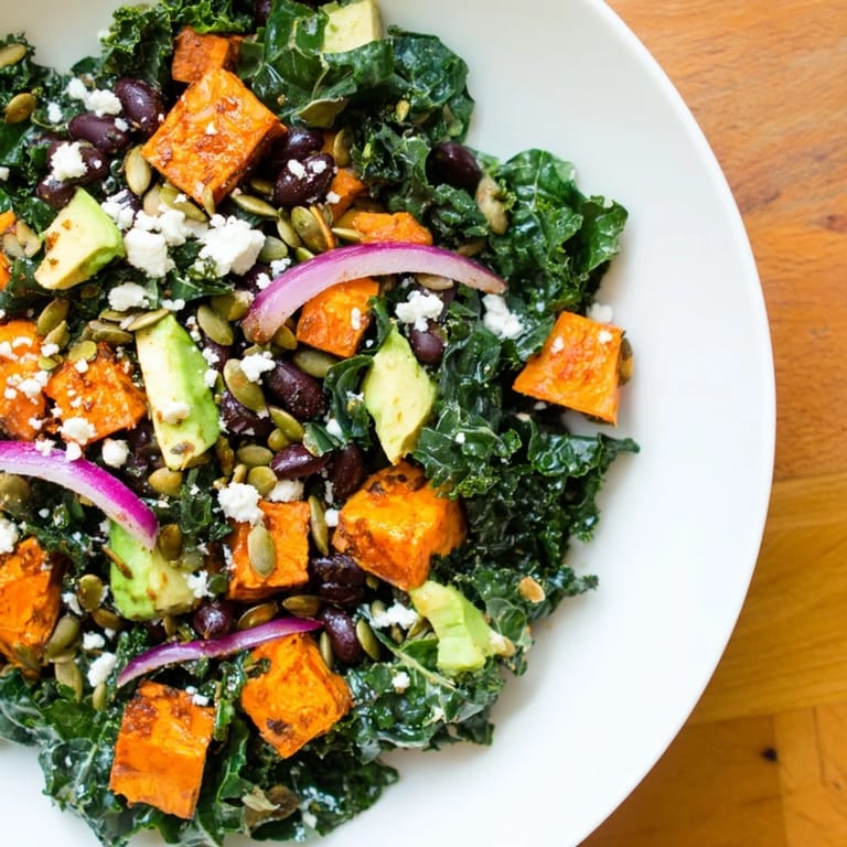 A colorful bowl of massaged kale salad, featuring avocado and red onion, with a zesty lime dressing.