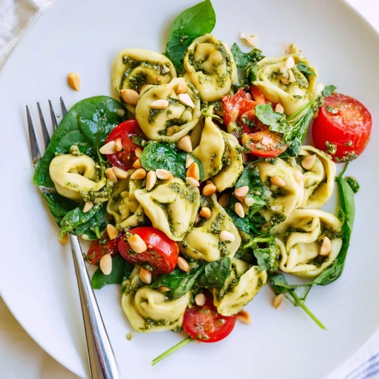 This chilled Pesto Tortellini Salad showcases plump tortellini coated in green pesto, dotted with halved red tomatoes and torn spinach.  